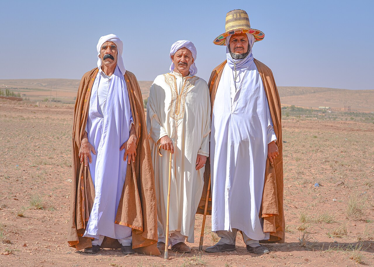 Trois hommes en tenue traditionnelle dans la wilaya de Djelfa ; deux portent un burnous brun.