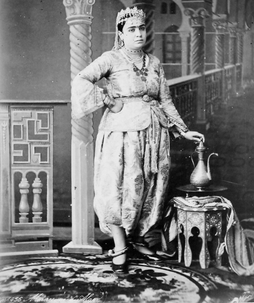 Algéroise portant un kwiyet à manches évasées avec un pantalon bouffant, dans un portrait ancien en noir et blanc.