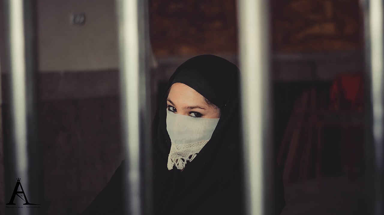 Portrait contemporain en m’laya noire et voilette blanche, photographié en Algérie.