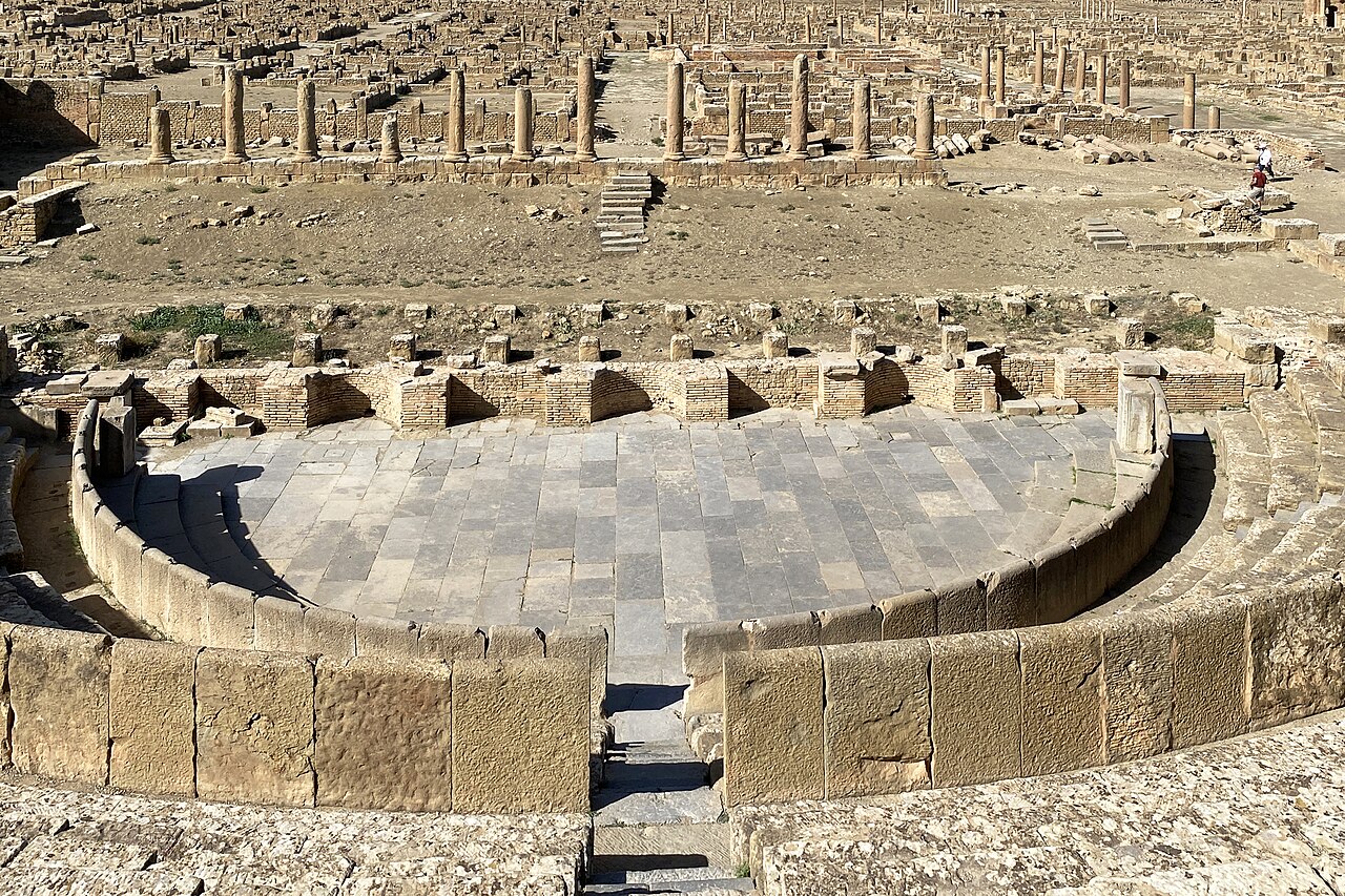 Théâtre antique de Timgad, avec ses gradins en pierre et les ruines de la ville à l’arrière-plan.